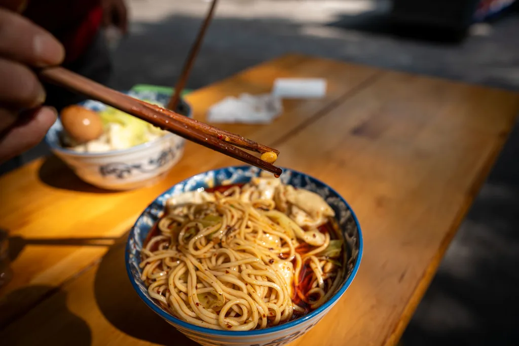 A bowl of spicy Chongqing xiaomian noodles being lifted with chopsticks