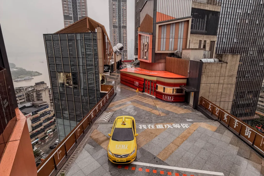 A yellow taxi navigating a steep street between old Chongqing buildings